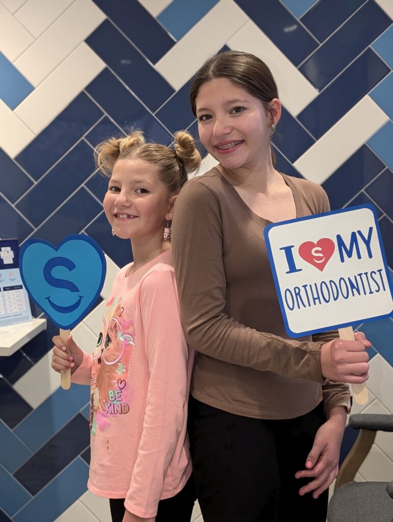 Two teen patients smiling holding 'i love my orthodontist' sign at Senties Ortho